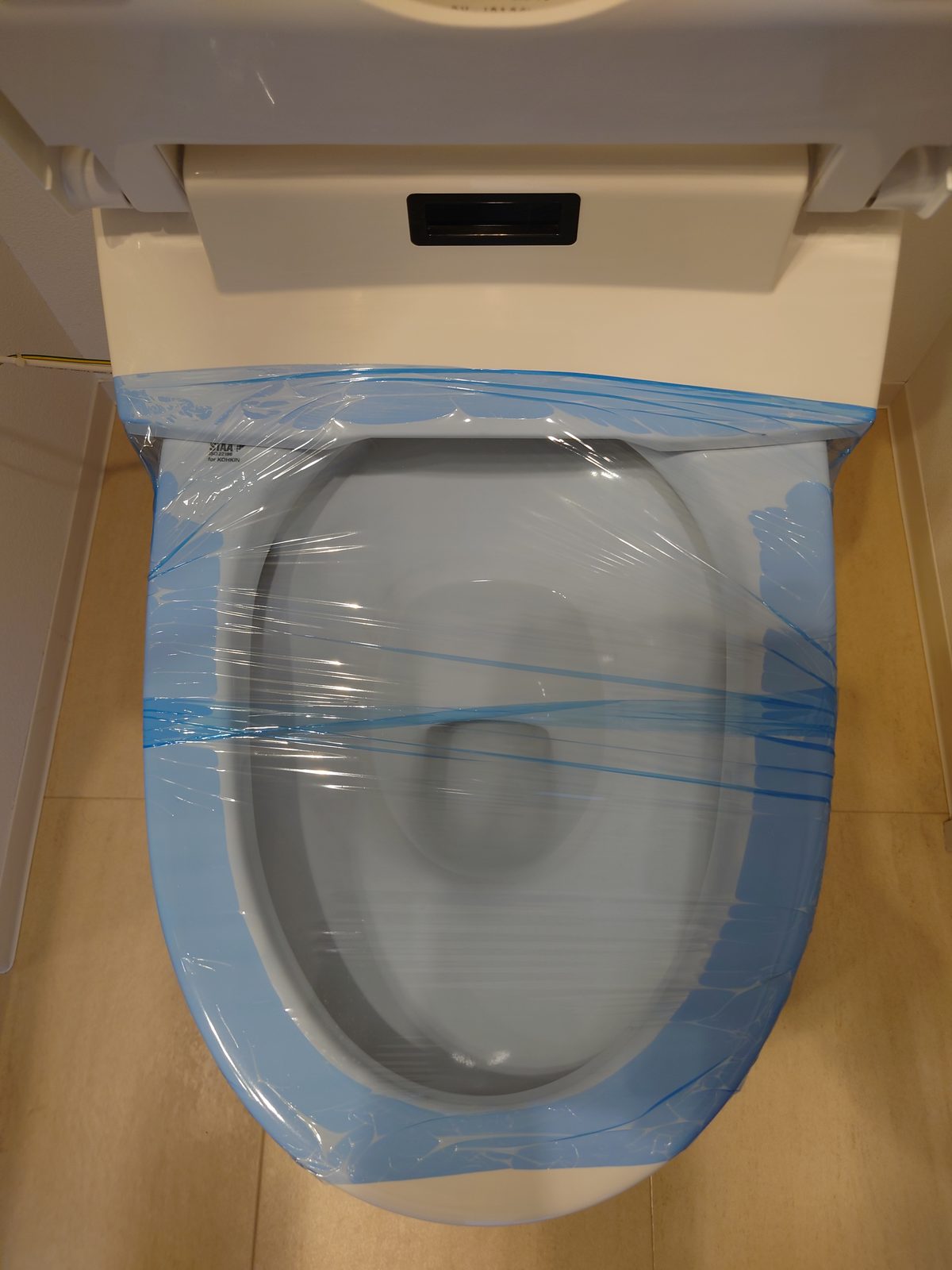 入居前の便器。便座と蓋を上げて、便器の縁ごと青い養生フィルムで覆われている